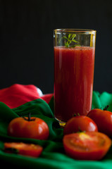 Glass and bottle of tomato juice with vegetables and green napkin on wooden background