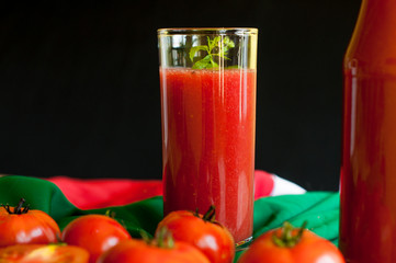 Glass and bottle of tomato juice with vegetables and green napkin on wooden background