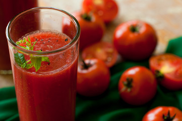 Glass and bottle of tomato juice with vegetables and green napkin on wooden background