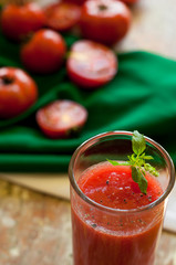 Glass and bottle of tomato juice with vegetables and green napkin on wooden background