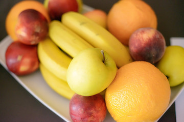 Oranges, apples, bananas and peaches on a white plate, with selective focus
