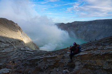 Woman sitting on top of crater Mount Kawah Ijen volcano is the largest sulfuric acidic lake in the world with smoke and fog,famous, popular and landmark travel destination in Java Island Indonesia.