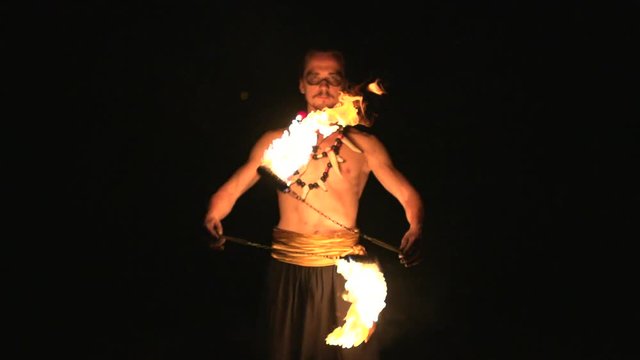 Fire show performance. Male fire performer spinning burning fire rope dart poi on long rope In front of his abs. Slow motion