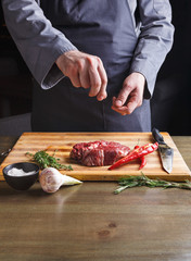 Chef seasoning rib eye steak on wooden board at restaurant kitchen