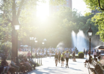 Anonymous crowds of people with sunlight shining through the trees in Washington Square Park in New York City