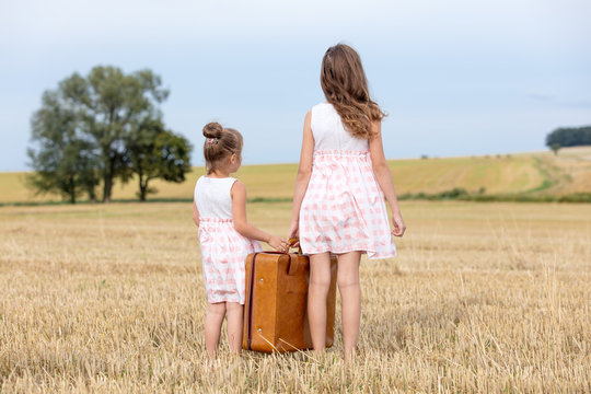 Two Little girls in classic dress holding suitcase