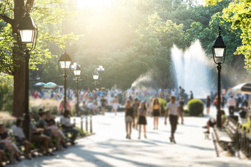 Anonymous crowds of people walking in Washington Square Park in New York City with the glow of...