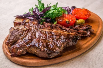 Gordijnen Appetizing steak on the bone, with tomatoes and herbs, on a wooden board. Horizontal frame © Алексей Еремеев