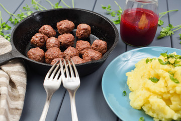 Homemade Sweden meatballs in cast iron pan served with mashed potatoes and red berry sauce with two forks side view