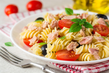 Fusilli pasta salad with tuna, tomatoes, black olives and basil on gray stone background