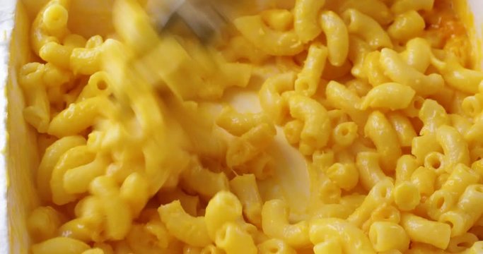 Video of macaroni and cheese in a microwavable paper tray being briskly stirred with a fork after heating.