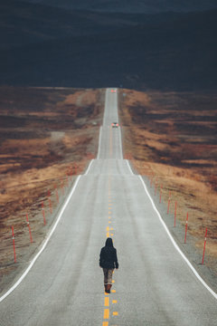 Woman walking away on an empty desolate road to Cape North, Norway.