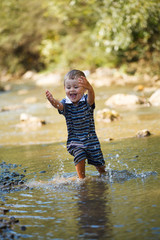 The little boy plays with the flow of water in the mountains, the summer nature is outdoors