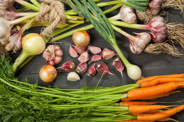 Fresh garlic, carrots and onions and vegetables on black wooden background