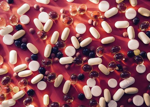 Assorted pharmaceutical medicine pills, tablets and capsules over red background