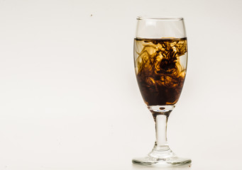 Dark brown food coloring diffuse in water inside wine glass with empty copyspace area for slogan or advertising text message, over isolated grey background. 