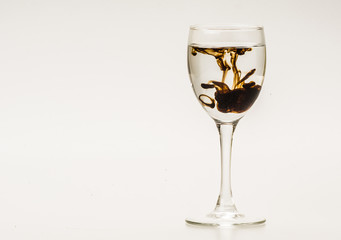 Dark brown food coloring diffuse in water inside wine glass with empty copyspace area for slogan or advertising text message, over isolated grey background. 