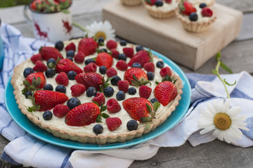 Fruit tart strawberries, blueberries, raspberries on wood in the garden view from above