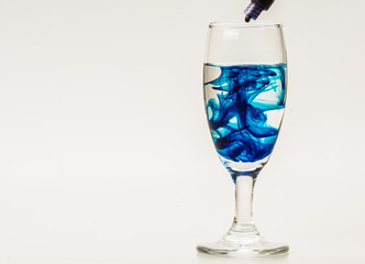 Blue food coloring diffuse in water inside wine glass with empty copyspace area for slogan or advertising text message, over isolated grey background. 