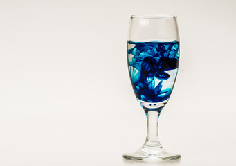 Blue food coloring diffuse in water inside wine glass with empty copyspace area for slogan or advertising text message, over isolated grey background. 