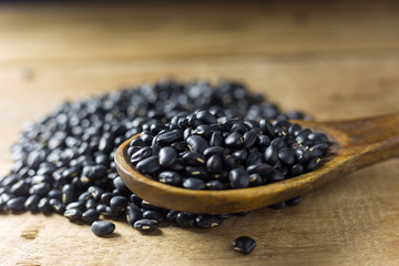 Sack of black beans spill beans with black beans in a wooden spoon on wooden table.