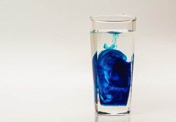 Blue food coloring diffuse in water inside glass with empty copyspace area for slogan or advertising text message, over isolated grey background. 
