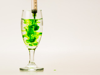 Green food coloring diffuse in water inside wine glass with empty copyspace area for slogan or advertising text message, over isolated grey background.