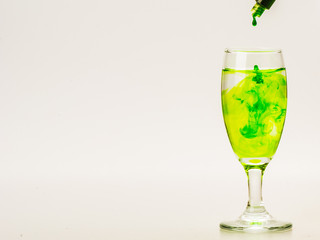 Green food coloring diffuse in water inside wine glass with empty copyspace area for slogan or advertising text message, over isolated grey background.