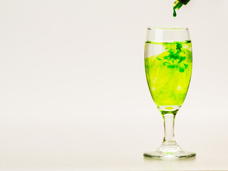 Green food coloring diffuse in water inside wine glass with empty copyspace area for slogan or advertising text message, over isolated grey background.