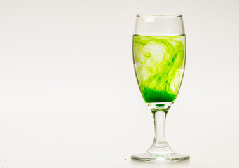 Green food coloring diffuse in water inside wine glass with empty copyspace area for slogan or advertising text message, over isolated grey background.