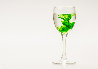 Green food coloring diffuse in water inside wine glass with empty copyspace area for slogan or advertising text message, over isolated grey background.