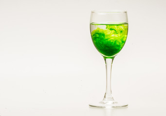 Green food coloring diffuse in water inside wine glass with empty copyspace area for slogan or advertising text message, over isolated grey background.