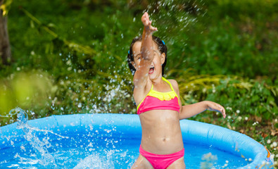 Little girl in an inflatable pool in the garden near the house
