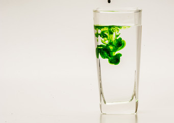 Green food coloring diffuse in water inside glass with empty copyspace area for slogan or advertising text message, over isolated grey background. 