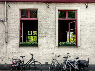 Fototapeta na wymiar Cute bikes parked against the white bricked wall of a tavern with open windows, red frames, flowers in them. Location: Belgium
