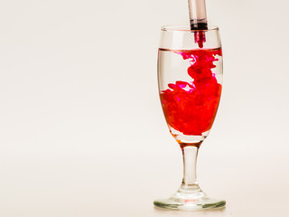 Red food coloring diffuse in water inside wine glass with empty copyspace area for slogan or advertising text message, over isolated grey background. 