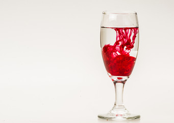 Red food coloring diffuse in water inside wine glass with empty copyspace area for slogan or advertising text message, over isolated grey background. 