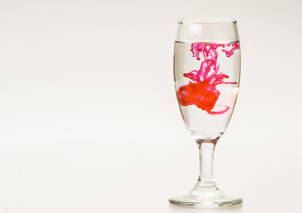 Red food coloring diffuse in water inside wine glass with empty copyspace area for slogan or advertising text message, over isolated grey background. 