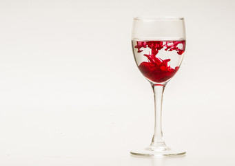 Red food coloring diffuse in water inside wine glass with empty copyspace area for slogan or advertising text message, over isolated grey background. 
