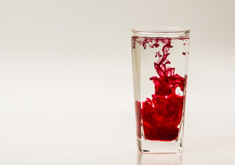 Red food coloring diffuse in water inside glass with empty copyspace area for slogan or advertising text message, over isolated grey background. 