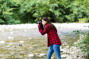 Female model in plaid shirt taking a photo with a camera near the river