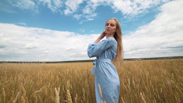 A young girl in a blue dress is standing in the field, and the wind is fluttering her hair