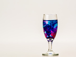 mixture of food coloring diffuse in water inside wine glass with empty copyspace area for slogan or advertising text message, over isolated grey background. 