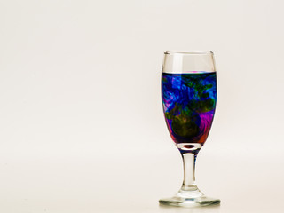 mixture of food coloring diffuse in water inside wine glass with empty copyspace area for slogan or advertising text message, over isolated grey background. 