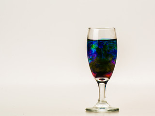 mixture of food coloring diffuse in water inside wine glass with empty copyspace area for slogan or advertising text message, over isolated grey background. 