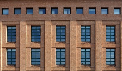 
Brick facade of a modern building with wide  windows and a row of small square windows at the top
