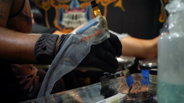 Tattoo artist dipping the machine needle into disposable ink cup. Man working on black gloves in tattoo salon. Slow motion.
