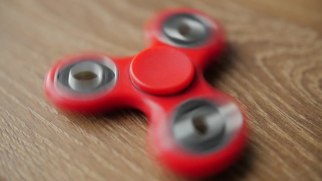 Red fidget spinner spinning on a wooden table. Close up.