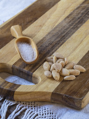 salted almonds with wooden scoop with salt on wooden cutting board