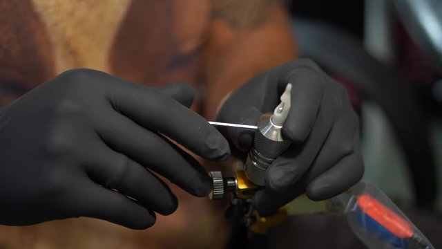 Male artist prepares tools and machine for tattoo session, man holding a tattoo gun. Master works in black sterile gloves. Slow motion. The tattooist checks the machine for performance
